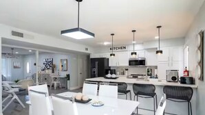 Una cocina moderna con gabinetes blancos, una isla central e iluminación colgante.