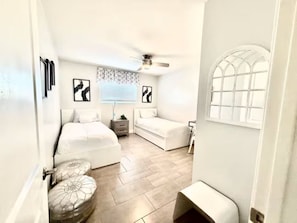 Ein kleines Schlafzimmer mit Bett, einer Sitzecke, einem Deckenventilator und einem Fenster mit Gittermuster.