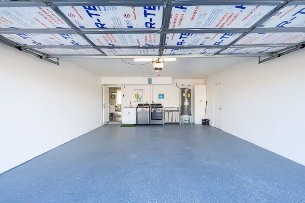 A spacious indoor area with a blue floor, a ceiling with metal beams and insulation panels, and a kitchen area in the background.
