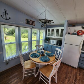 A dining area with a round table set for four, white chairs, and a view of the outdoors through large windows.