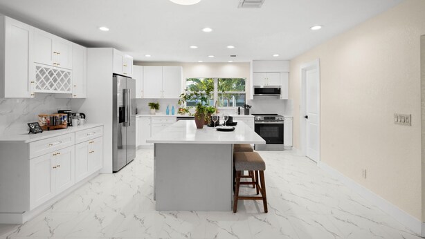 A modern kitchen with white cabinetry, a central island, stainless steel appliances, and a view of greenery outside. - 4-bedroom house in amazing Punta Gorda with cool vibes (Punta Gorda)