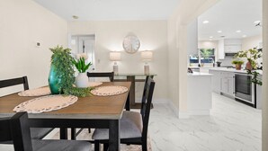 A dining area with a wooden table, chairs, a vase with plants, wall-mounted lamps, and a clock. - 4-bedroom house in amazing Punta Gorda with cool vibes (Punta Gorda)