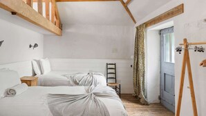 A bedroom with two beds, a wooden ladder, a small table, and a door with a curtain. - Hideaway on Dartmoor, Uphill Coach House (Lustleigh)