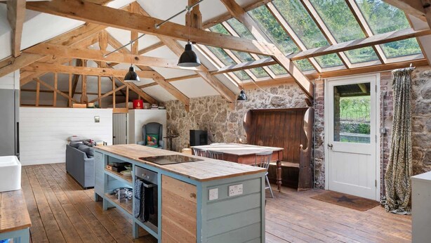 A rustic kitchen with wooden beams, a stone wall, and a large window. - Hideaway on Dartmoor, Uphill Coach House (Lustleigh)