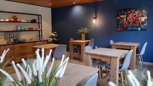 A dining area with wooden tables and chairs, a potted plant, and a wall-mounted light fixture.