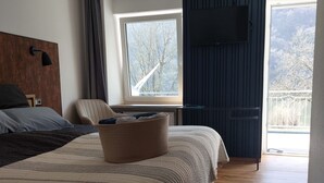 A bedroom with a large bed, a chair, a window with a view, and a TV mounted on the wall.