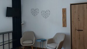 A room with two chairs, a small table, a TV mounted on the wall, and a wooden wardrobe.