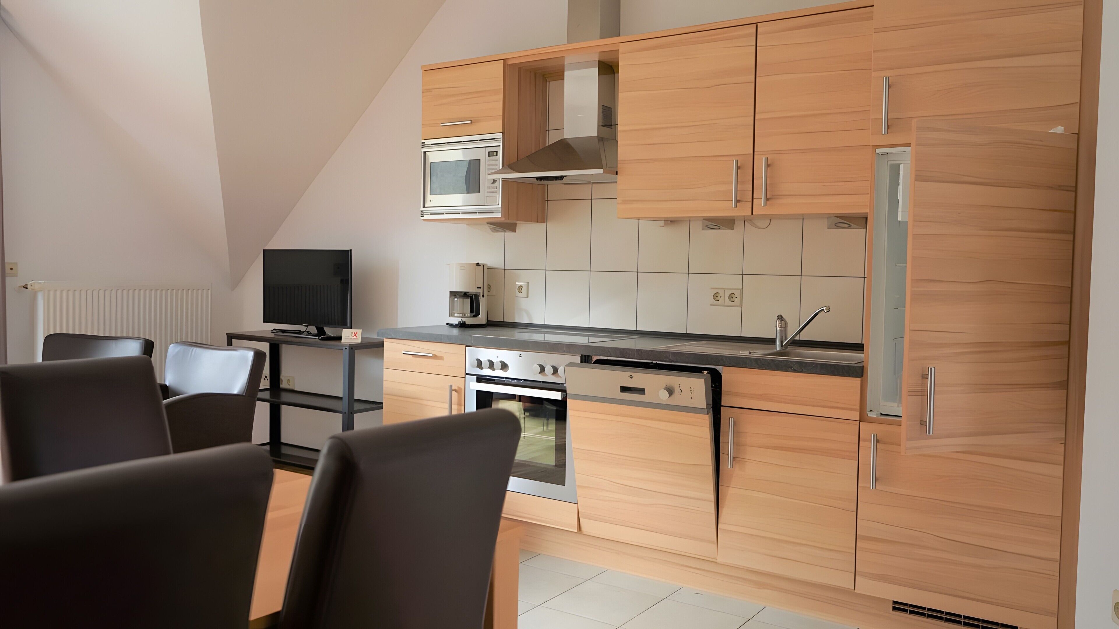 Eine moderne Küche mit Holzausstattung, einem Backofen, einer Mikrowelle und einem Kühlschrank. Es gibt einen Essbereich mit Stühlen und einem Tisch.