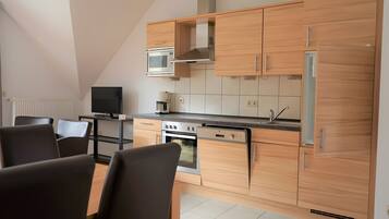 Eine moderne Küche mit Holzausstattung, einem Backofen, einer Mikrowelle und einem Kühlschrank. Es gibt einen Essbereich mit Stühlen und einem Tisch.
