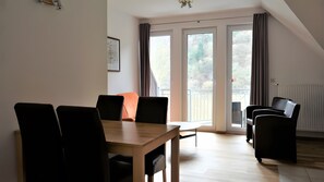 Et moderne værelse med et træspisebord, sorte stole, en sofa og en balkon med gelænder.