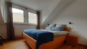 Et soveværelse med en træseng, et natbord, et vindue med gardiner og en radiator.