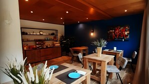 En restaurant med træborde og stole, en disk med forskellige ting, og en blå væg med et farverigt kunstværk.