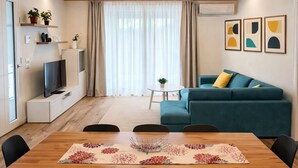 Una sala moderna con una mesa de comedor de madera, sillas negras, un sofá color turquesa y un televisor sobre un mueble blanco.