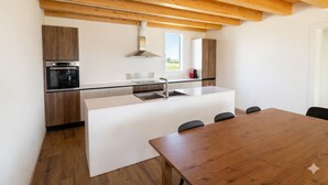Una cocina moderna con armarios de madera, horno empotrado, una isla grande con lavamanos y una mesa de comedor con sillas.