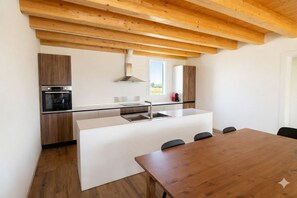 Eine moderne Küche mit Holzausbau, einem eingebauten Backofen, einer großen Kochinsel mit Spüle und einem Esstisch mit Stühlen.