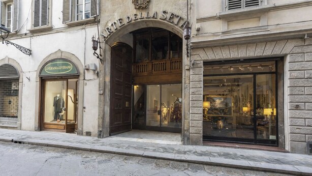 A building with an arched entrance labeled 'ARTE DELLA SETA,' a storefront with 'LIVERANO & LIVERANO' signage, and a large glass window displaying furniture. - Fossi Panoramic Terrace by MMega (Florence)