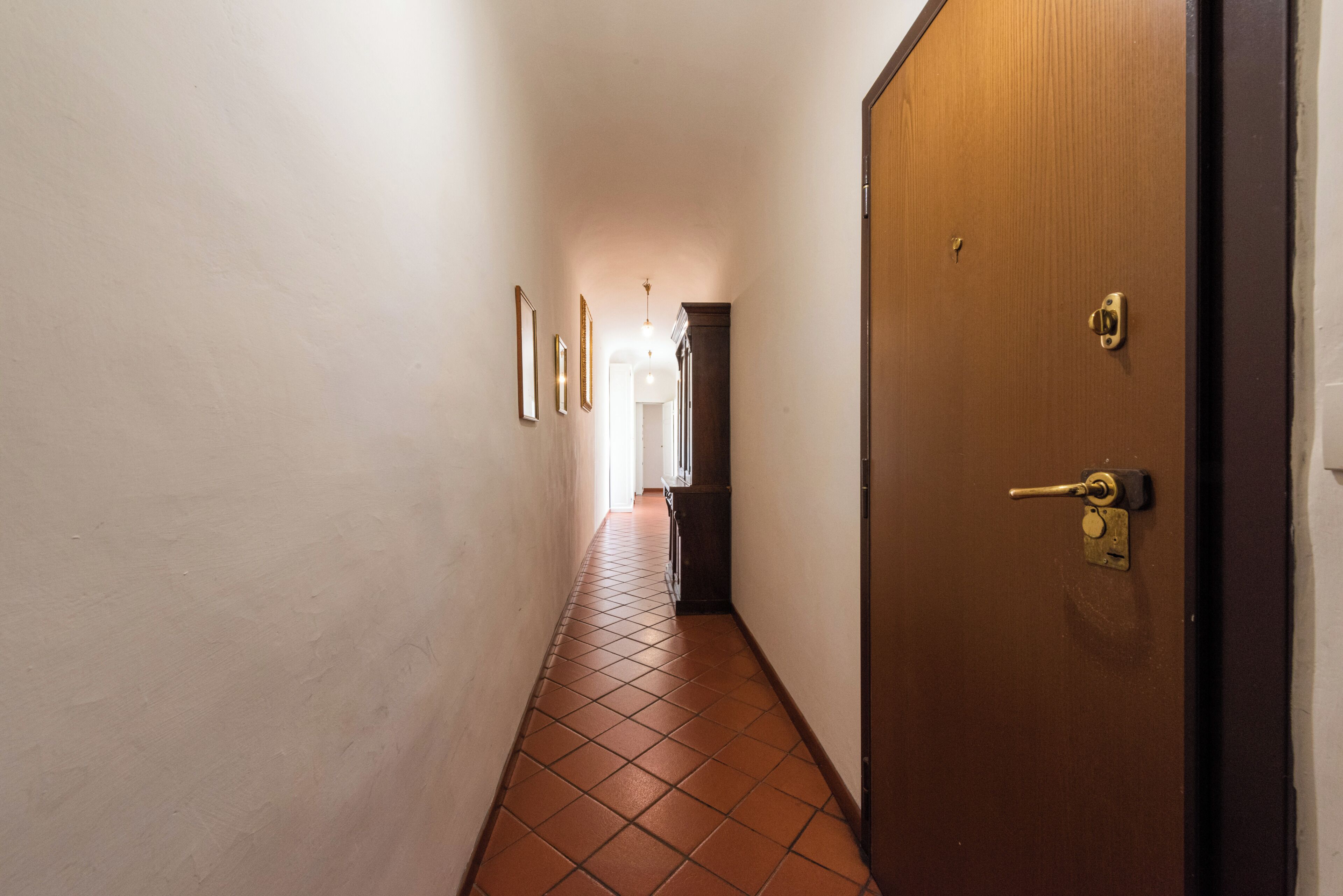 Un couloir avec une porte en bois, un sol carrelé et des tableaux encadrés accrochés au mur.
