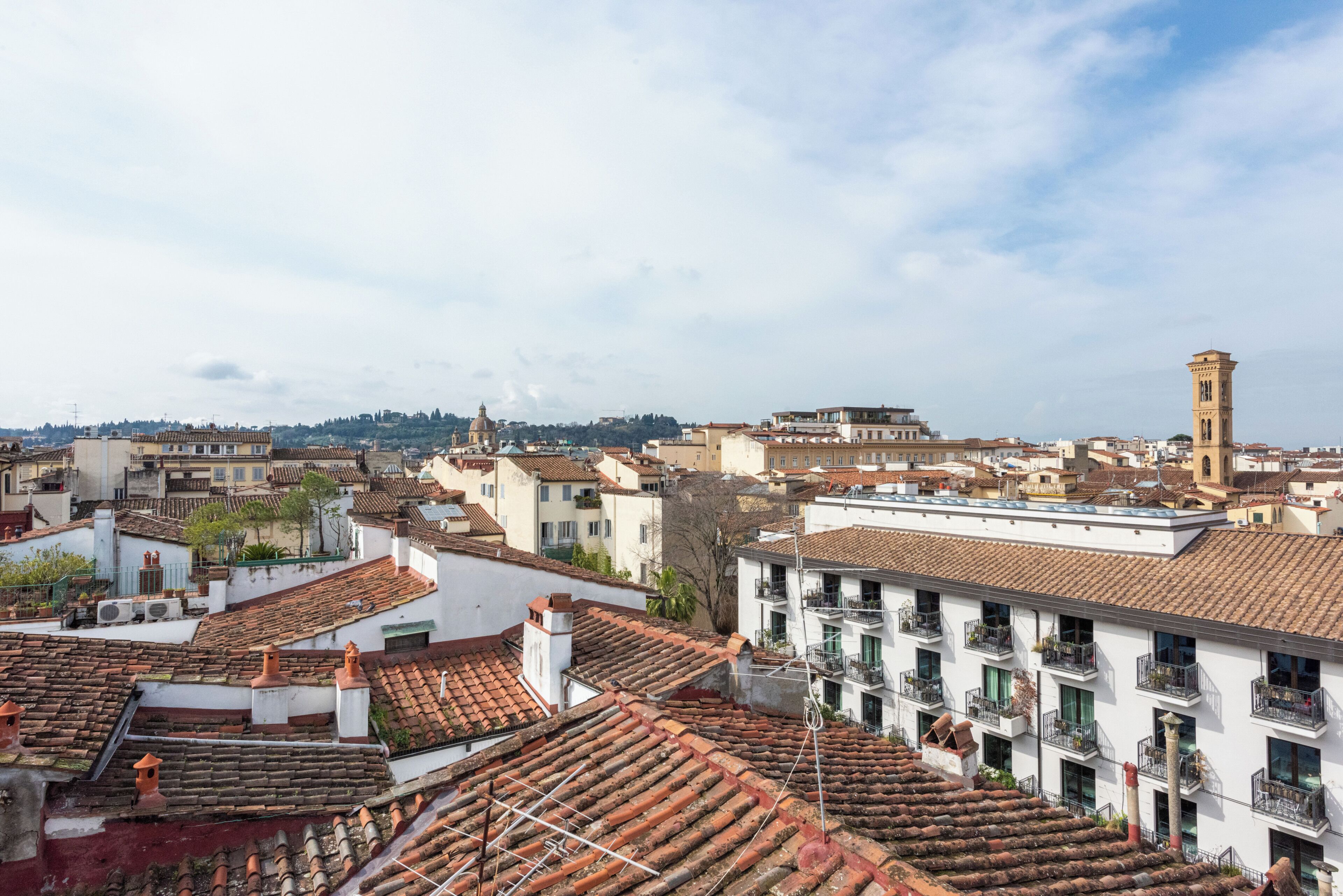 A cityscape with terracotta-tiled rooftops, a prominent tower, and a mix of residential and commercial buildings.