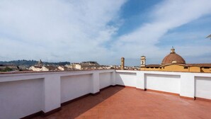 A rooftop terrace with terracotta flooring, white walls, and a view of distant buildings and a dome structure. - Fossi Panoramic Terrace by MMega (Florence)