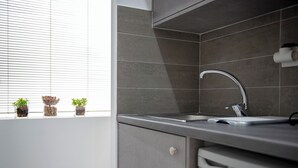 Eine moderne Küche mit Spüle aus Edelstahl, grauen Fliesen und einem Fenster mit Blumentöpfen.