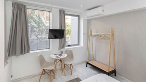 Ein Hotelzimmer mit Bett, Wandfernseher, Schreibtisch mit Stühlen, Kleiderständer aus Holz und einem Fenster mit Vorhängen.