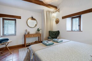 Een slaapkamer met een bed, een dressoir, een stoel, een spiegel en een raam.