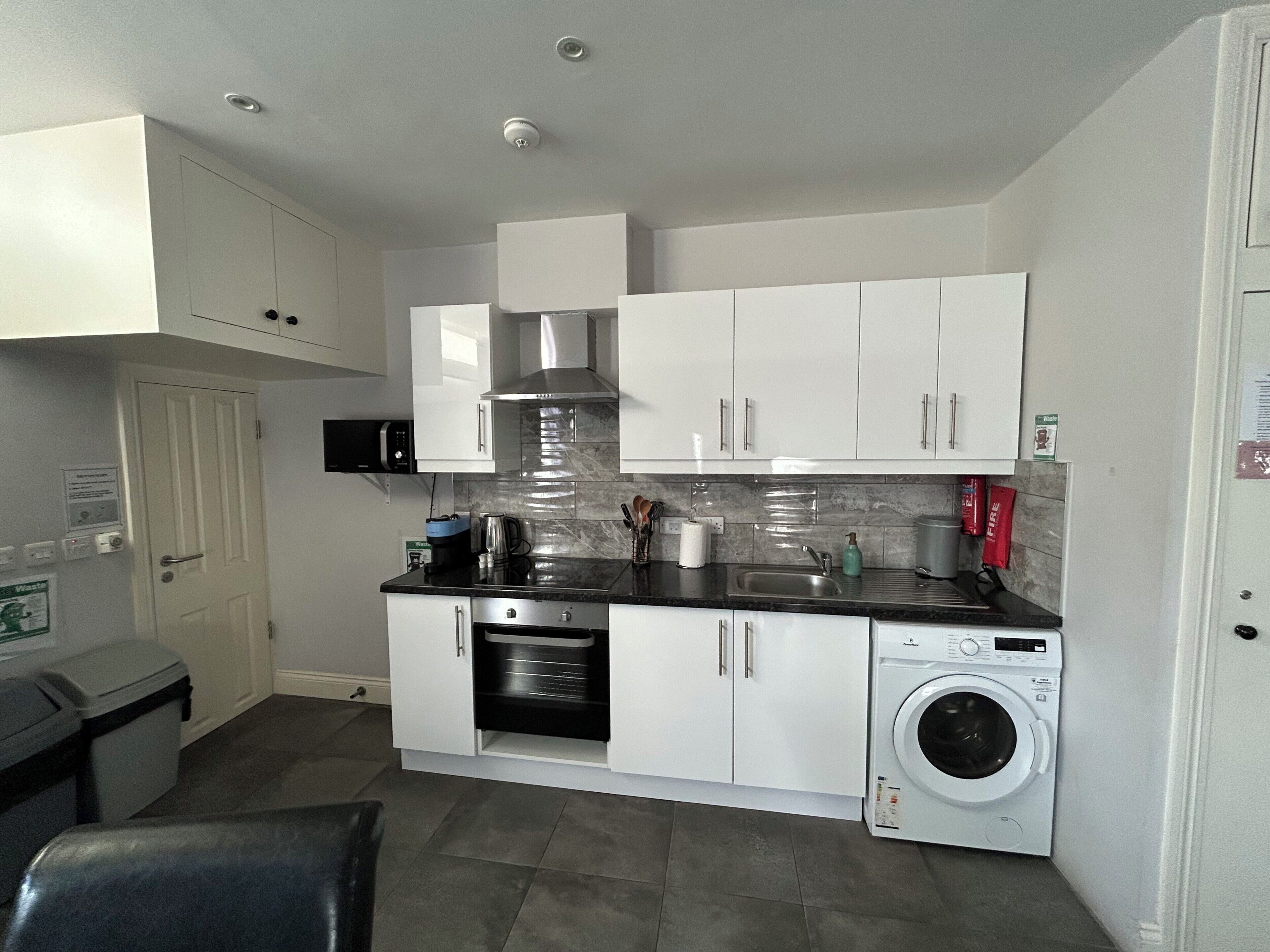 A compact kitchen with white cabinets, a microwave, a stove, and a washing machine.