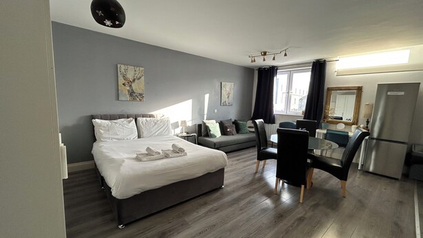 Ein modernes Hotelzimmer mit Bett, Sofa, Esstisch mit Stühlen, Kühlschrank und Bildern an der Wand.