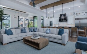 A modern living room with a sectional sofa, a coffee table, and a kitchen area with a grill. - New! Luxury Cape Coral Villa w/ Pool, Spa & Dock (Cape Coral)