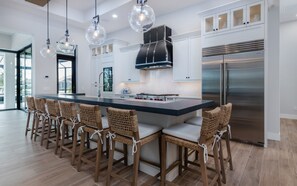A modern kitchen with a central island, stainless steel appliances, and wicker bar stools. - New! Luxury Cape Coral Villa w/ Pool, Spa & Dock (Cape Coral)