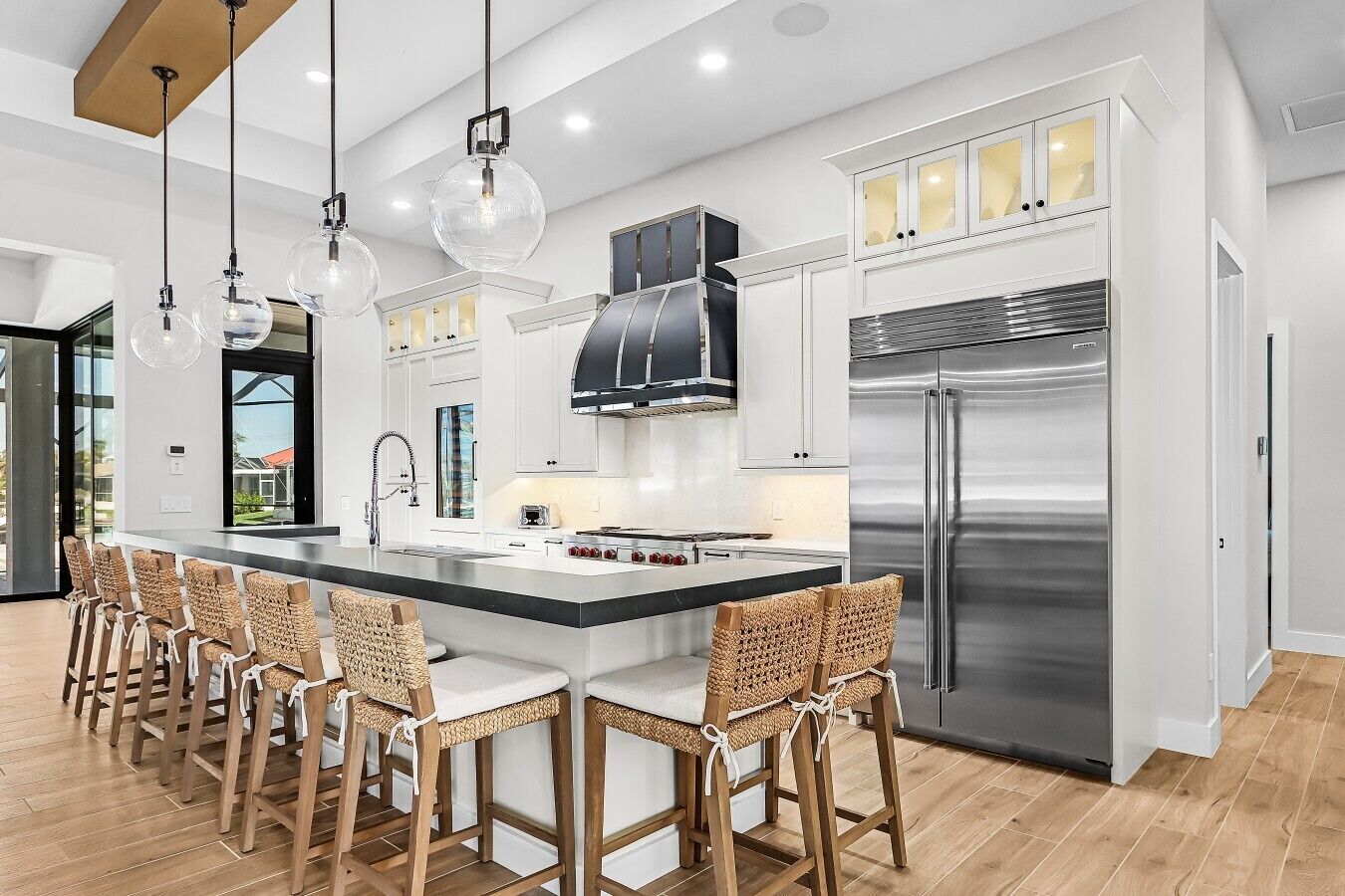 A modern kitchen with a central island, stainless steel appliances, and a seating area with woven chairs.