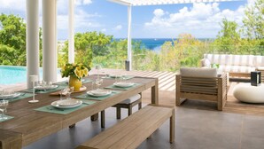 A dining area with a view of the ocean, a pool, and outdoor furniture. - Amara 4 - Luxury villa with sea view (Les Trois-Îlets)