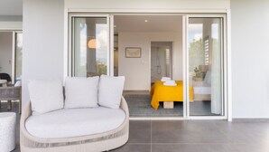 Une chambre moderne avec un grand canapé, un lit recouvert d’une housse de couette jaune et une porte-fenêtre coulissante donnant sur une salle de bain.