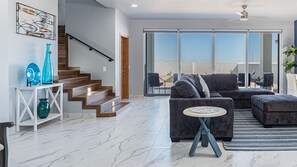 A modern living room with a staircase, a large sliding glass door leading to a balcony, and a sectional sofa. - Casa Bonita (Puerto Peñasco)