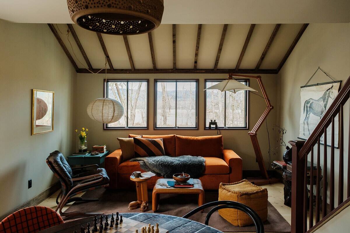 A cozy living room with a sofa, a coffee table, a chessboard, and a large window with a view of trees.