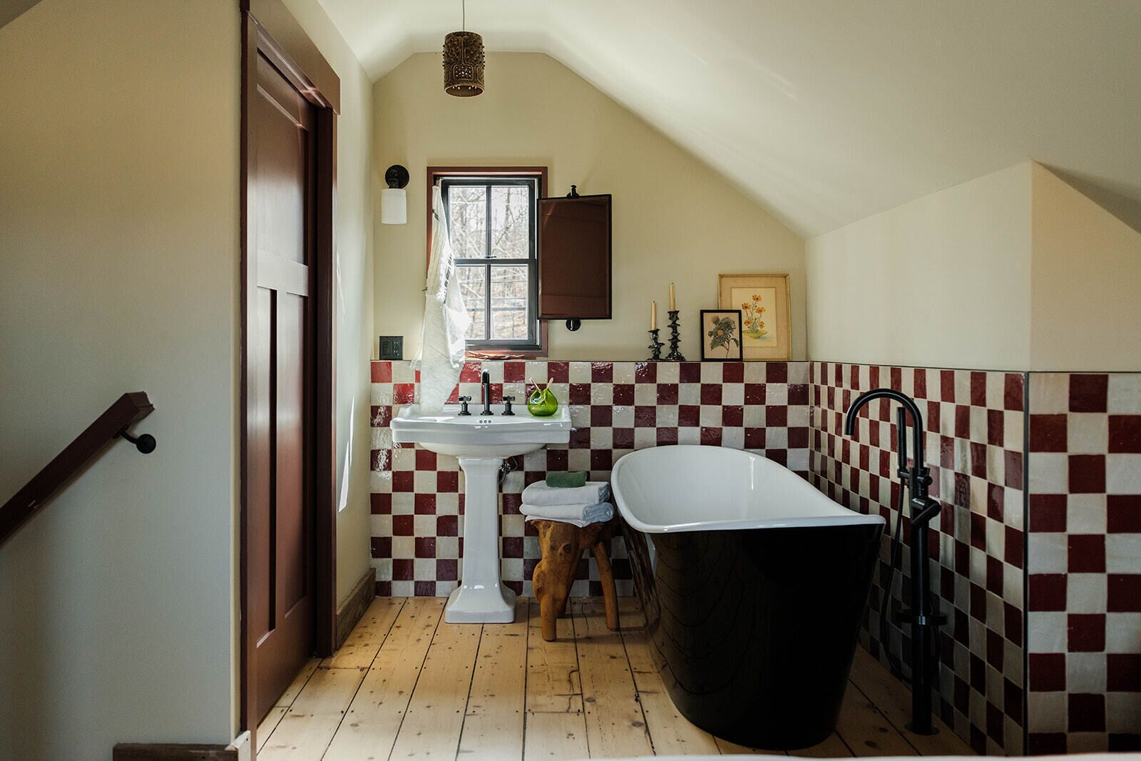 Une salle de bain avec un mur recouvert de carreaux à motifs, un lavabo blanc, une baignoire et un tabouret en bois.