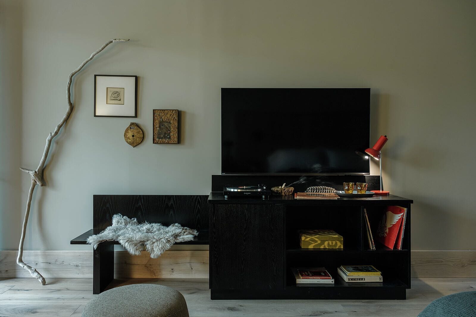 A modern living room with a flat-screen TV, a black entertainment unit, and a branch decoration.