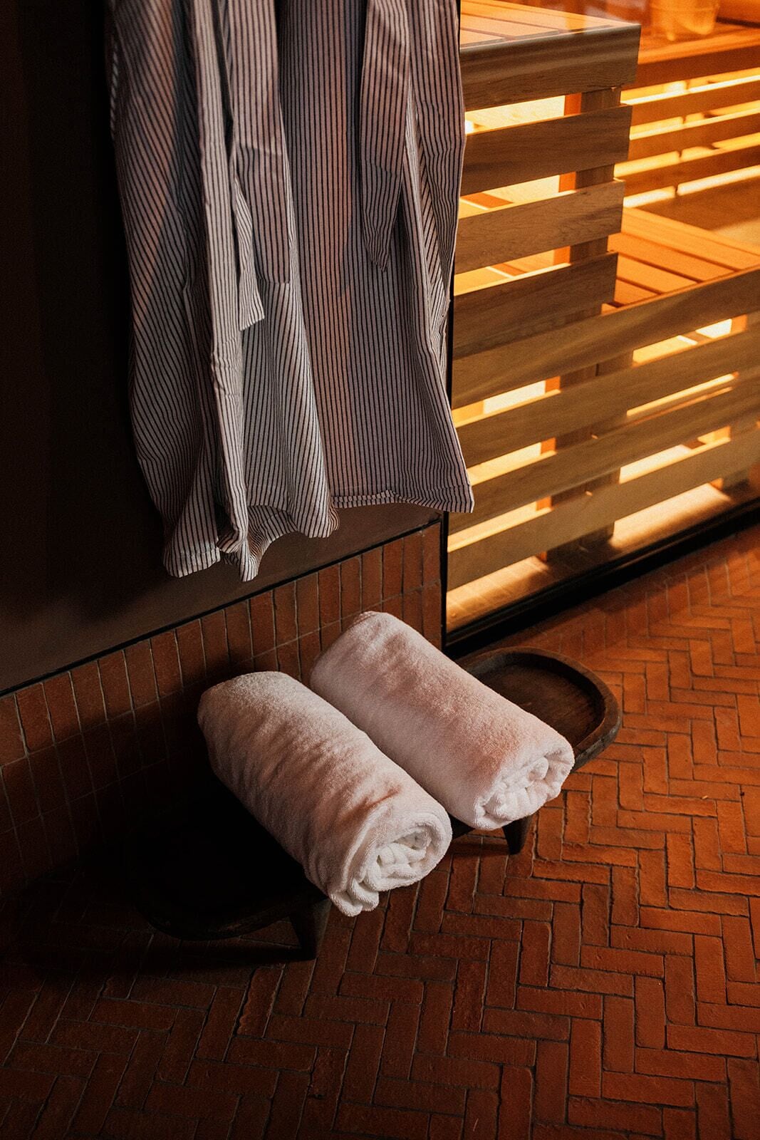 A room with a wooden bench, a towel rack with striped towels, and a brick floor.