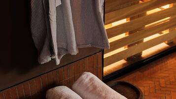 A room with a wooden bench, a towel rack with striped towels, and a brick floor.