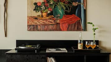 A room with a painting of flowers, a record player, a bottle, and glasses on a table.