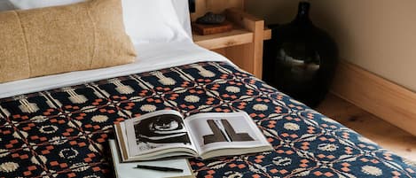A bed with a patterned bedspread, a book, and a pen on it.