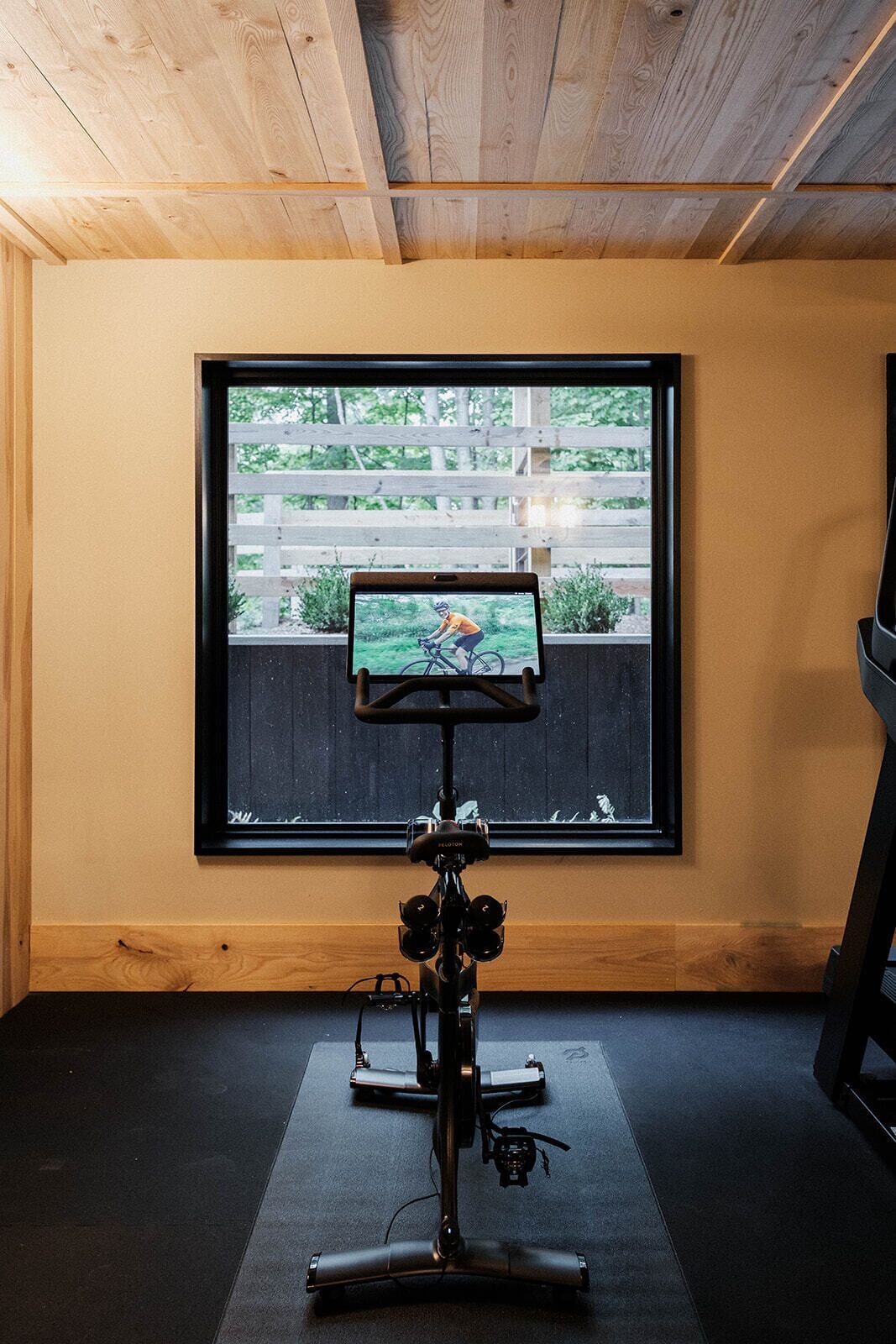 A room with a large window, a treadmill, and a television mounted on the wall.