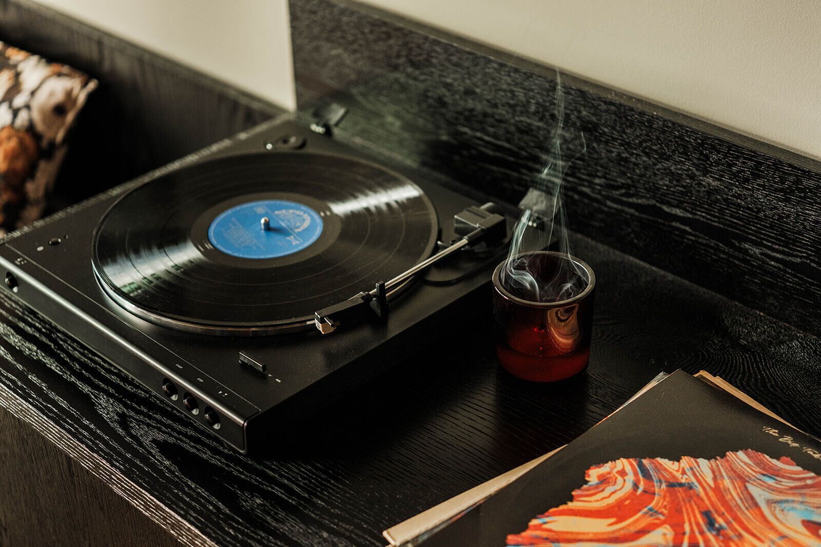 Tocadiscos con un disco de vinilo, un vaso con bebida y un libro sobre una superficie de madera.