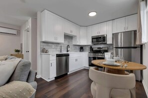 A modern kitchen with white cabinets, stainless steel appliances, and a dining area with a round wooden table and chairs. - Bright Studio Walkable Olde Towne East Parking (Columbus)