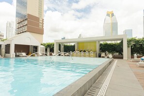 Ein Schwimmbecken mit Liegestühlen und Bar, umgeben von Hochhäusern.