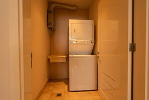 Een kleine wasruimte met een wasmachine, een droger, een klein wasbakje en een ventilatieopening in de muur.