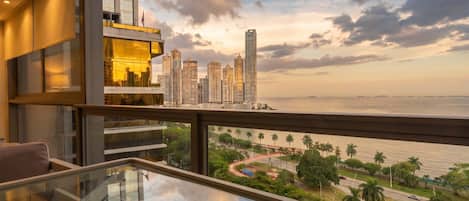 A modern hotel room with a balcony overlooking a city skyline and a body of water.