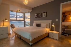 A bedroom with a large bed, bedside tables, a chair, and a view of the sea. - 13 E, Apartamento en YOO con vista al mar y 2 dormitorios (Panamá)