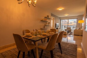 A dining area with a glass table, chairs, and a chandelier. There is a balcony with a view of the sky. - 13 E, Apartamento en YOO con vista al mar y 2 dormitorios (Panamá)