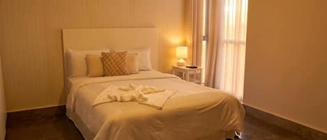 Una habitación de hotel con una cama, una mesita de noche con lámpara y una ventana con cortinas.